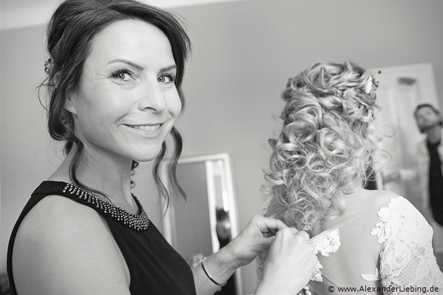 Hochzeitsfotograf Eventschloss Schönfeld - Freundin hilft Braut das Kleid hinten zu schließen