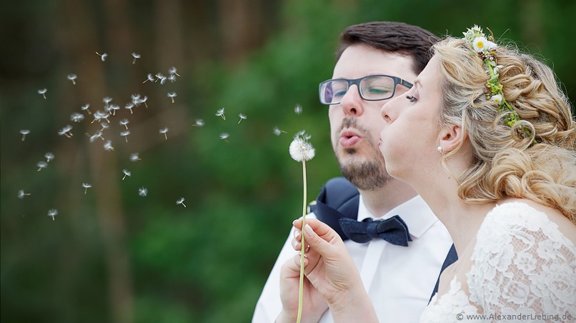 Hochzeit - Brautpaar Hochzeitsfotograf Eventschloss Schönfeld - Gemeinsam eine Pusteblume wegpusten
