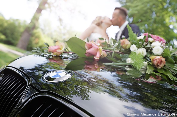 Hochzeit - Brautpaar Hochzeitsfotograf Standesamt Magdeburg / Gartenhaus im Stadtpark - Brautpaar küsst sich, im Vordergrund BMW