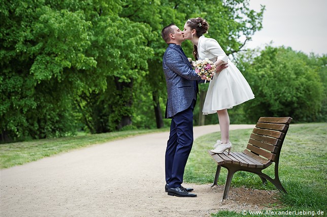 Hochzeit - Brautpaar Hochzeitsfotograf Standesamt Magdeburg / Elbelandhaus - Braut steht auf Bank und küsst Bräutigam, der davor steht.