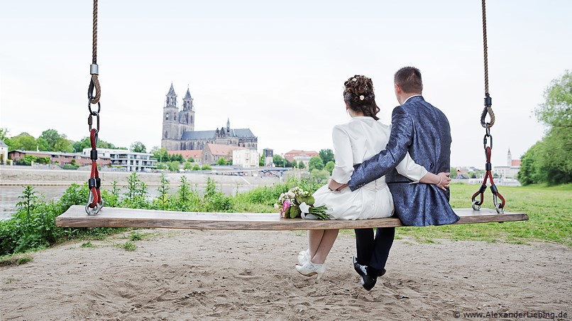 Hochzeitsfotograf Standesamt Magdeburg / Elbelandhaus - Brautpaar sitzt auf Elbschaukel, schaut zum Magdeburger Dom