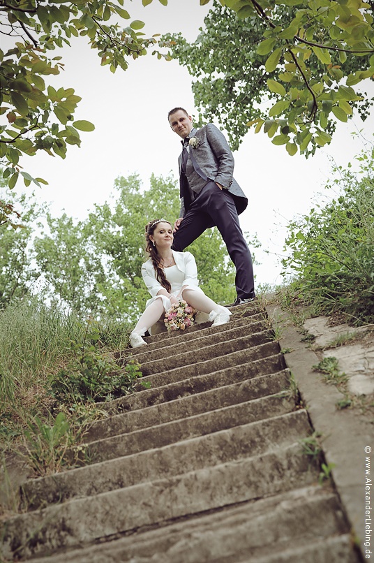 Hochzeit - Brautpaar Hochzeitsfotograf Standesamt Magdeburg / Elbelandhaus - Braut sitzt auf Treppe und Bräutigam steht dahinter.
