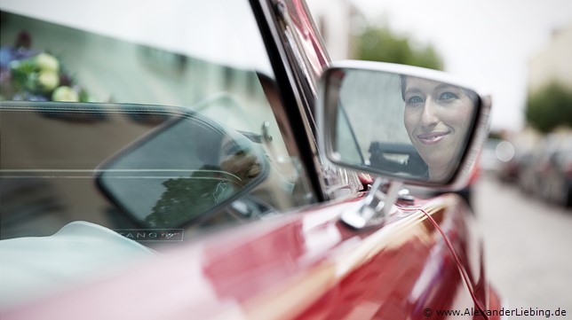 Hochzeit - kurz vor der Trauung Hochzeitsfotograf Standesamt Barleben / Robinien-Hof Gommern - ein Brautlächeln im Autospiegel des Ford Mustang
