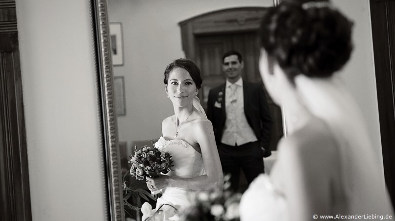 Hochzeit - Begrüßung, Sektempfang und Spielereien Hochzeitsfotograf Standesamt Barleben / Robinien-Hof Gommern - Braut lächeln über den Spiegel vor Ihr Ihren Bräutigam an