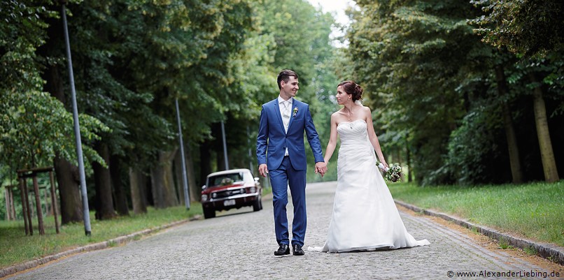 Hochzeit - Brautpaar Hochzeitsfotograf Standesamt Barleben / Robinien-Hof Gommern - Ehepaar spaziert Hand in Hand, Ford Mustang im Hintergrund
