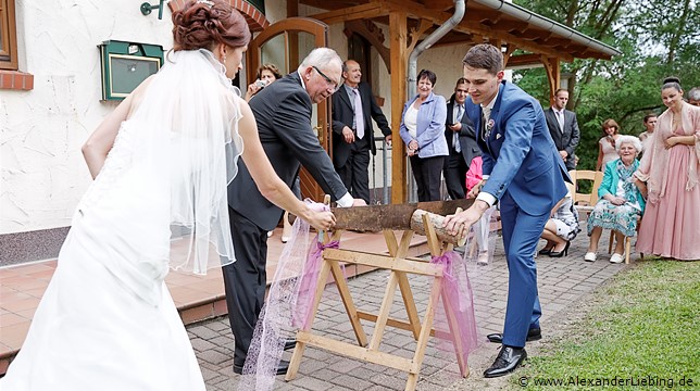 Hochzeitsfotograf Standesamt Barleben / Robinien-Hof Gommern - spielend schafft das Bautpaar trotz rostier Säge den Baumstamm durch zu sägen
